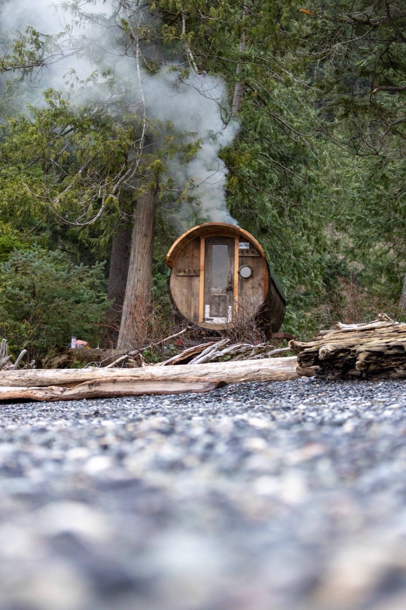 The restored barrel sauna with smoke rising from the chimney, seen from a pebble beach