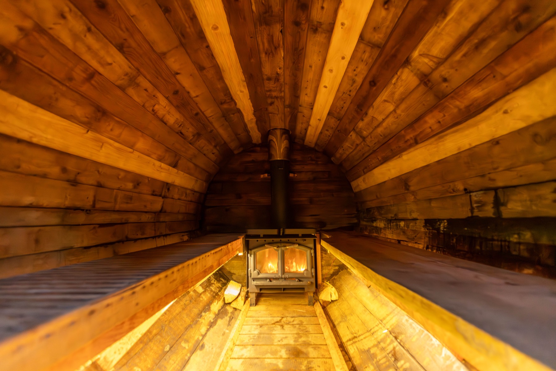 Warm cedar interior of the barrel sauna with benches and the wood stove